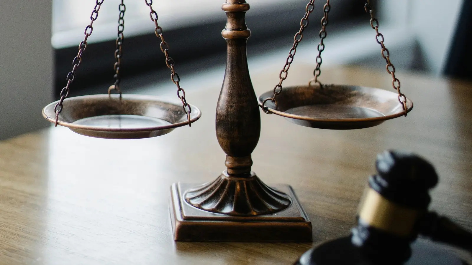 Brass scales of justice and a gavel on a wooden desk