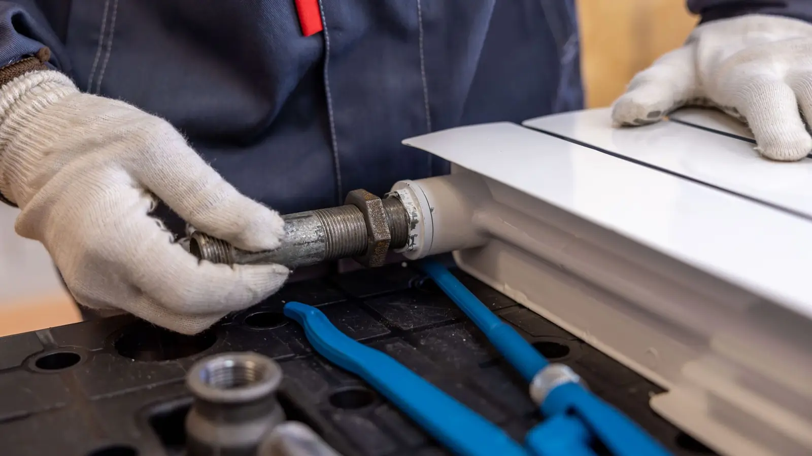Plumber’s gloved hands tightening a pipe fitting